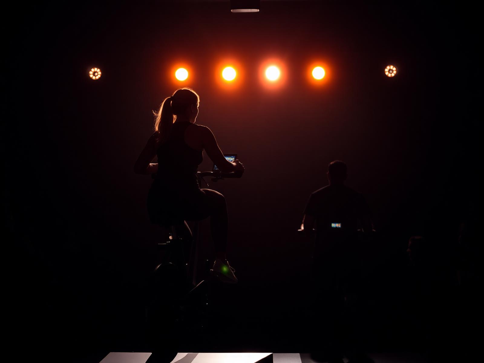 Instructor silhouetted on stage in a boutique cycling studio